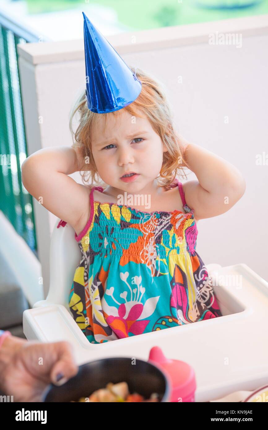 Deux ans enfant blonde avec un chapeau de fête en carton bleu blanc assis  dans une chaise haute à la recherche au sérieux Photo Stock - Alamy