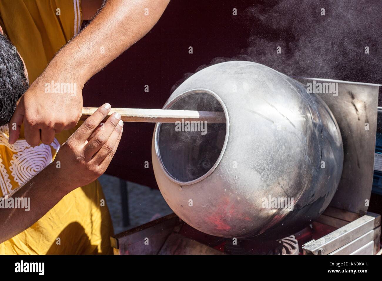 L'homme préparer les graines de tournesol enrobées de caramel avec longue cuillère en bois dans un pot rotatoire. Banque D'Images