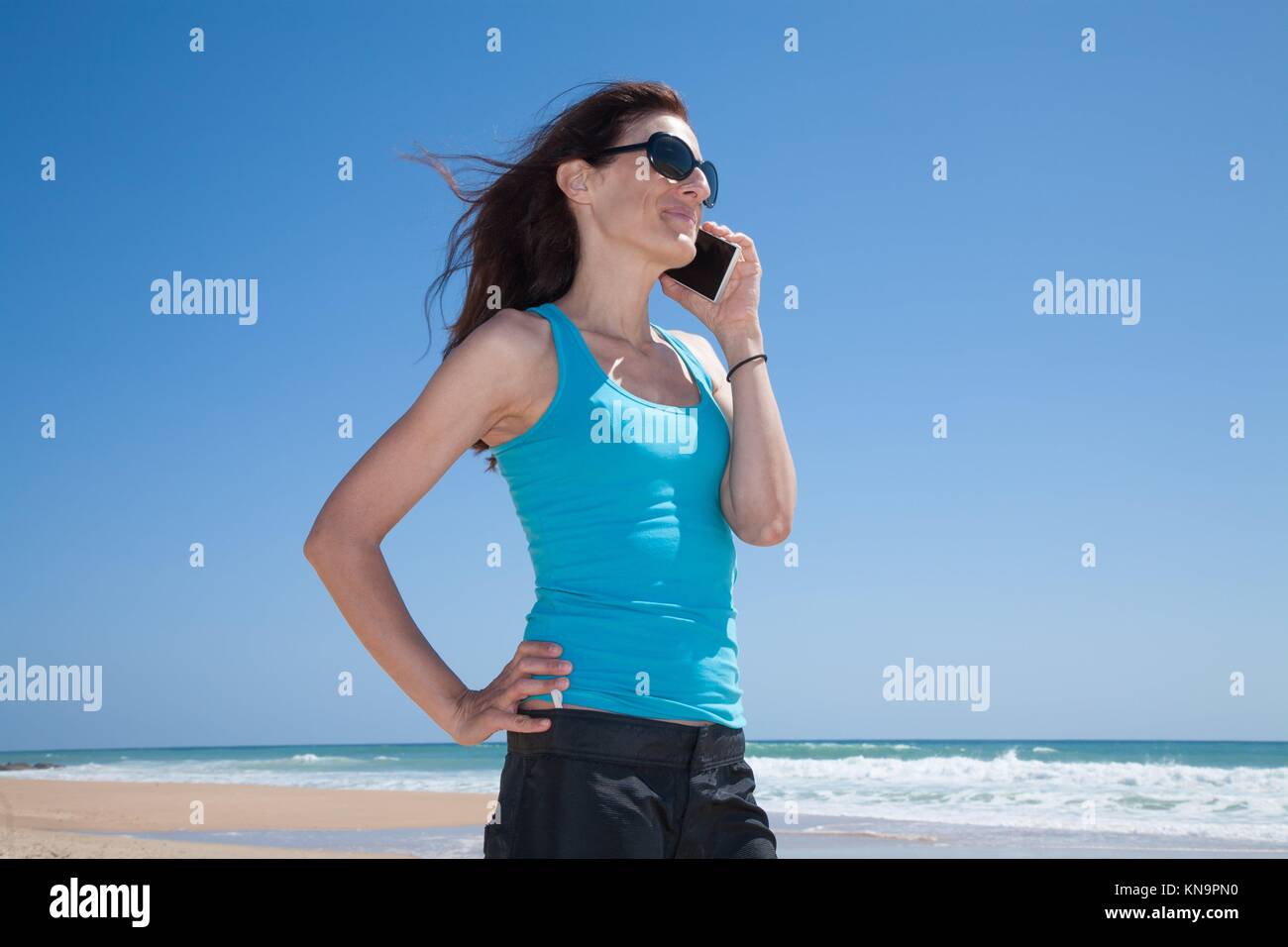 Portrait de profil de femme brune avec des lunettes noir et cyan bleu shirt  smiling and talking on mobile phone smartphone à plage Photo Stock - Alamy