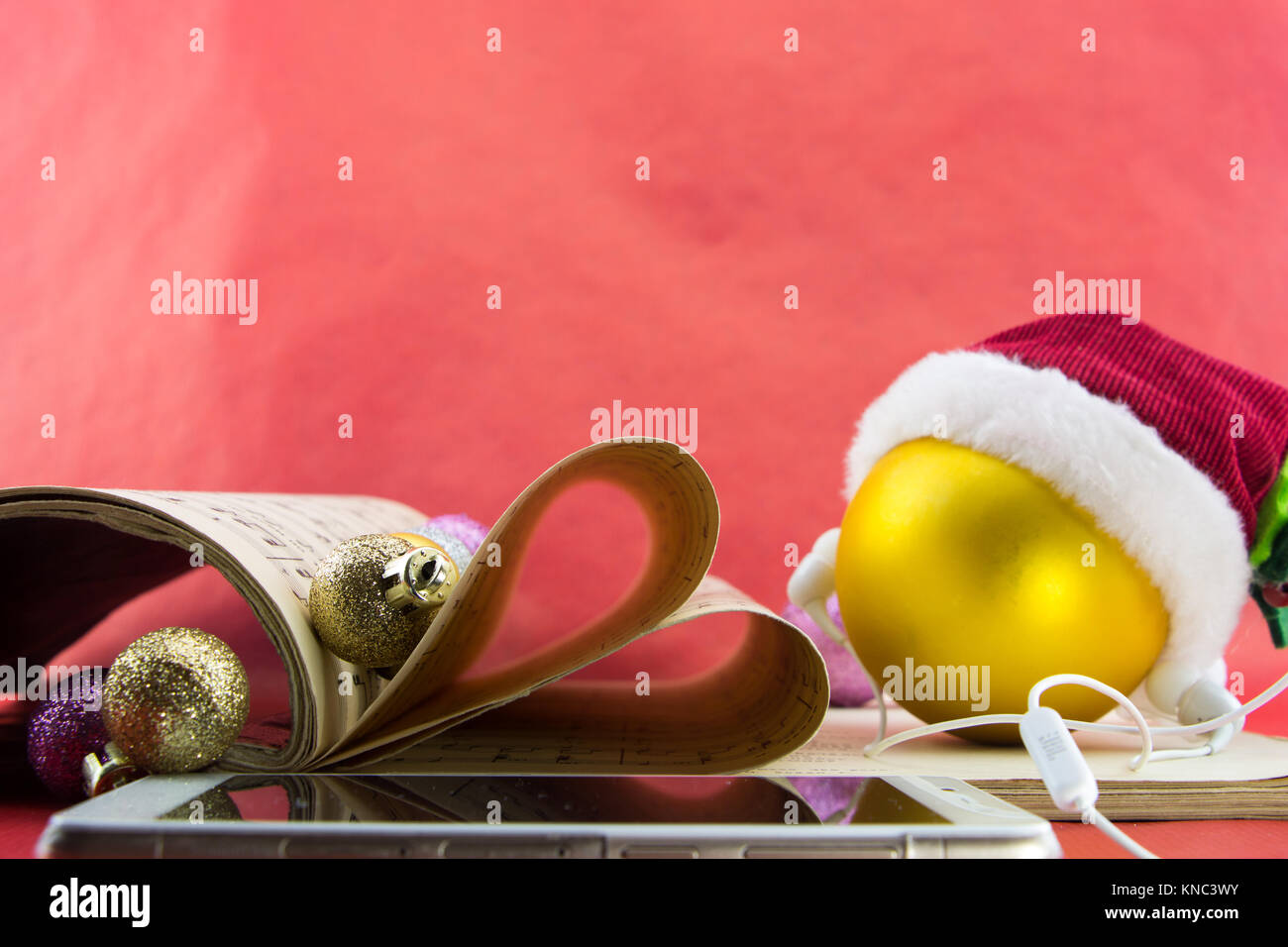 Boule de Noël avec Santa's hat et écouteurs, la notation musicale livre avec pages l'élaboration de coeur, sur fond rouge. Banque D'Images