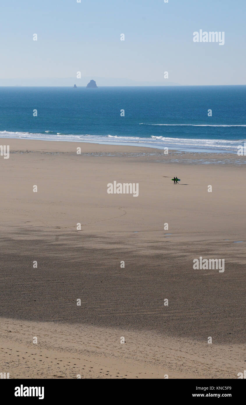 Deux surfeurs marchant sur une plage vide Rolvenden à Cornwall. Bawden Rocks sont à l'arrière-plan Banque D'Images