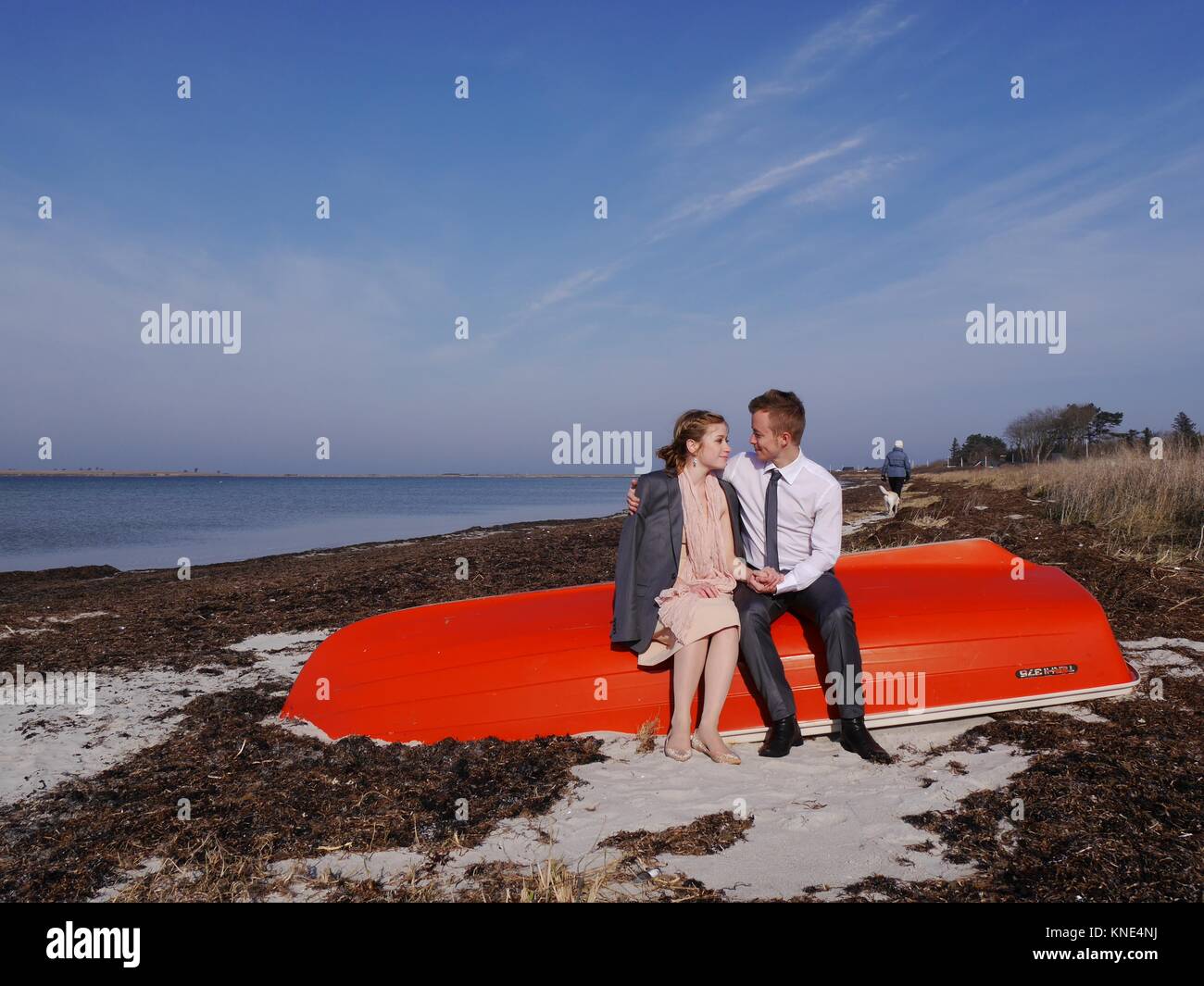 Jeune couple assis sur bateau rouge vif échoués en hiver sur l'île de Aero, au Danemark. Ils regardent dans les yeux et chacun avec sa veste de ses épaules rondes Banque D'Images