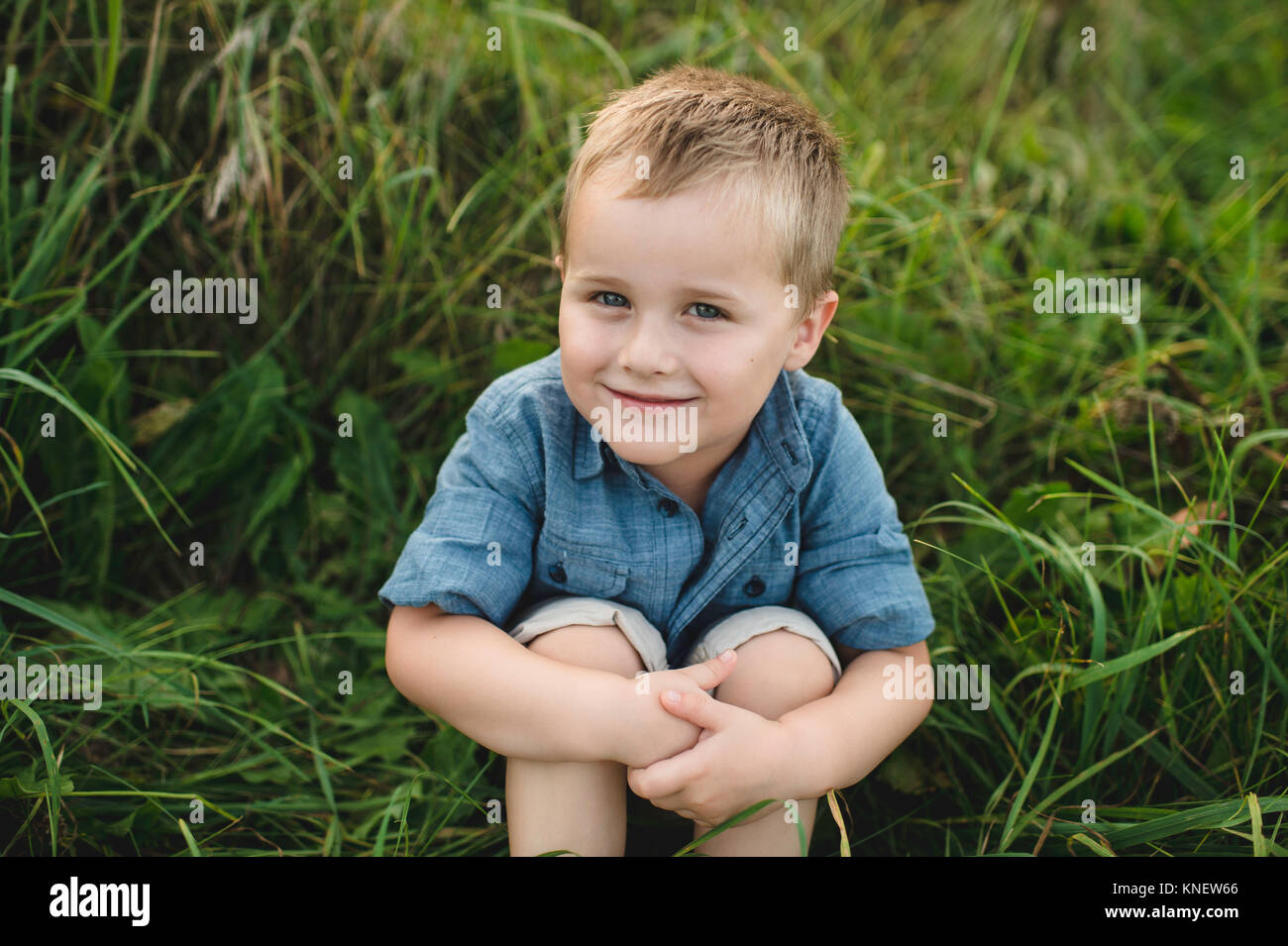 Portrait of smiling boy sitting in tall grass looking at camera Banque D'Images