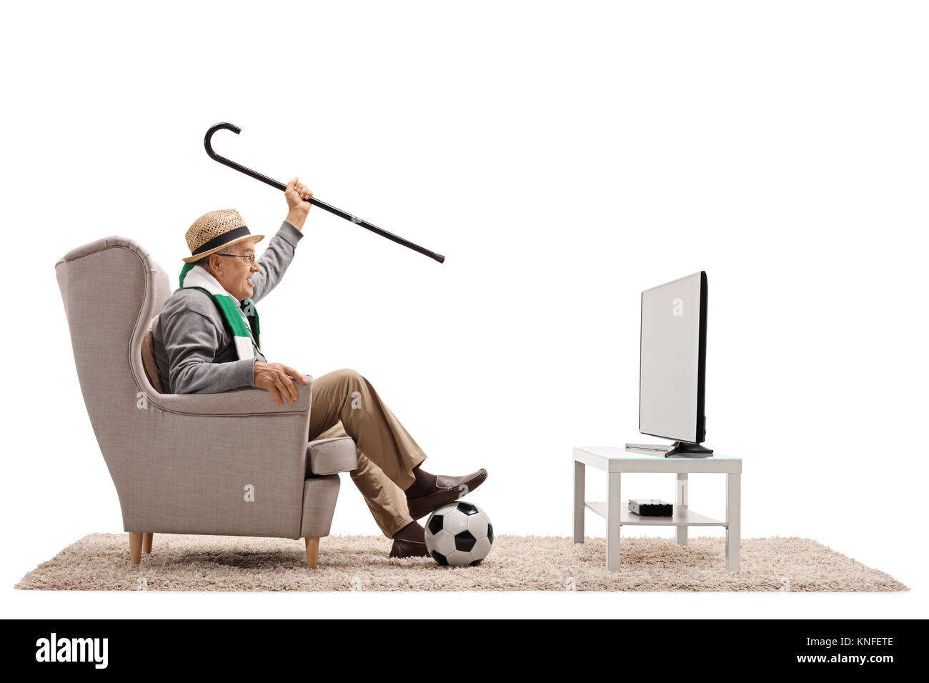 Personnes âgées heureux fan de foot avec un foulard et de canne à sucre assis dans un fauteuil à regarder la télévision isolé sur fond blanc Banque D'Images