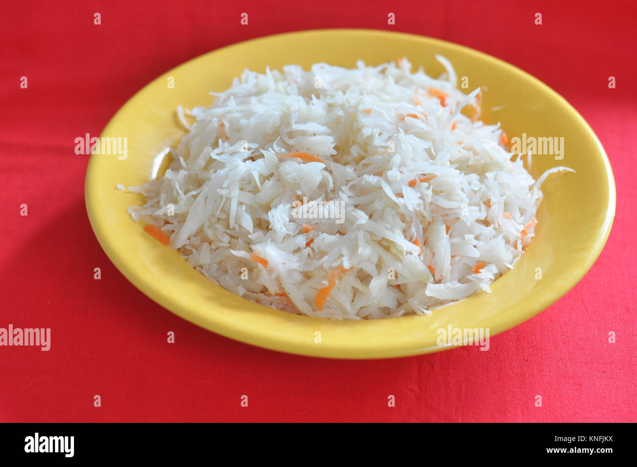 La choucroute avec les carottes dans une plaque jaune sur le fond rouge. Banque D'Images