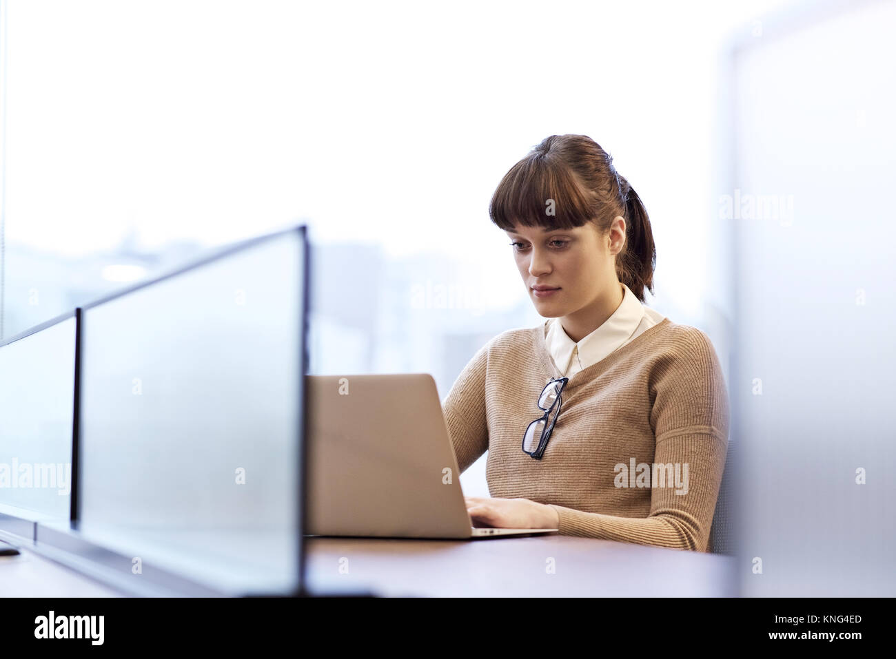 Caucasian female office worker assis à un bureau dans un bureau lumineux à l'aide d'un ordinateur portable le port de lunettes de lecture with copy space Banque D'Images