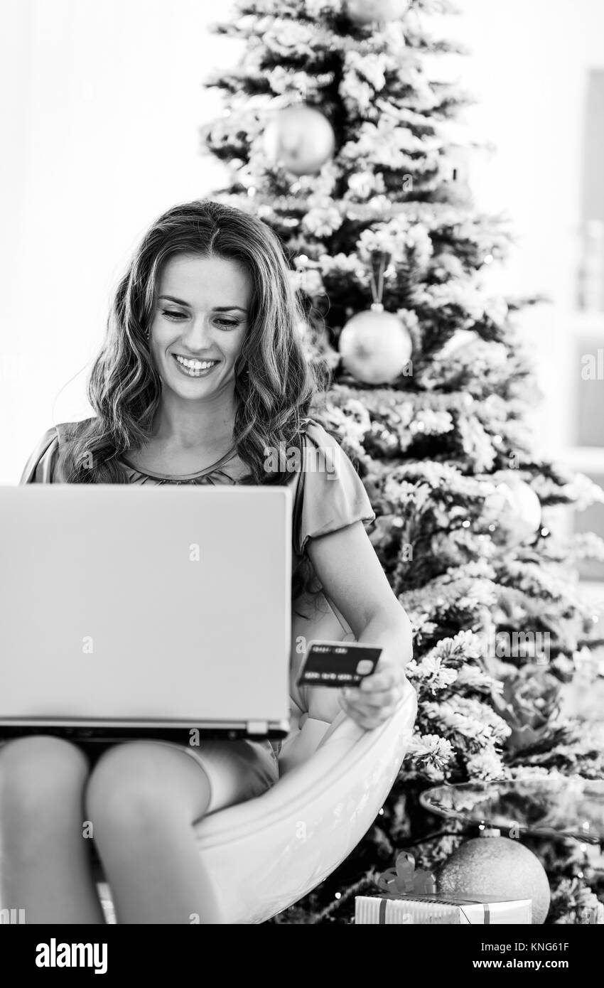 Portrait of smiling young woman with credit card using laptop near Christmas Tree Banque D'Images