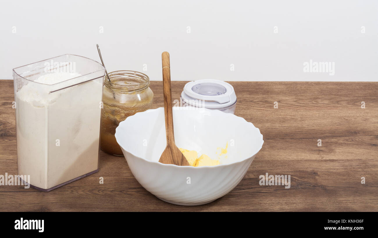 Ingrédients pour faire la pâte sucrée sur la table de la cuisine. La farine, le miel, le sucre et le beurre dans un bol blanc sur le beau fond de bois. Banque D'Images