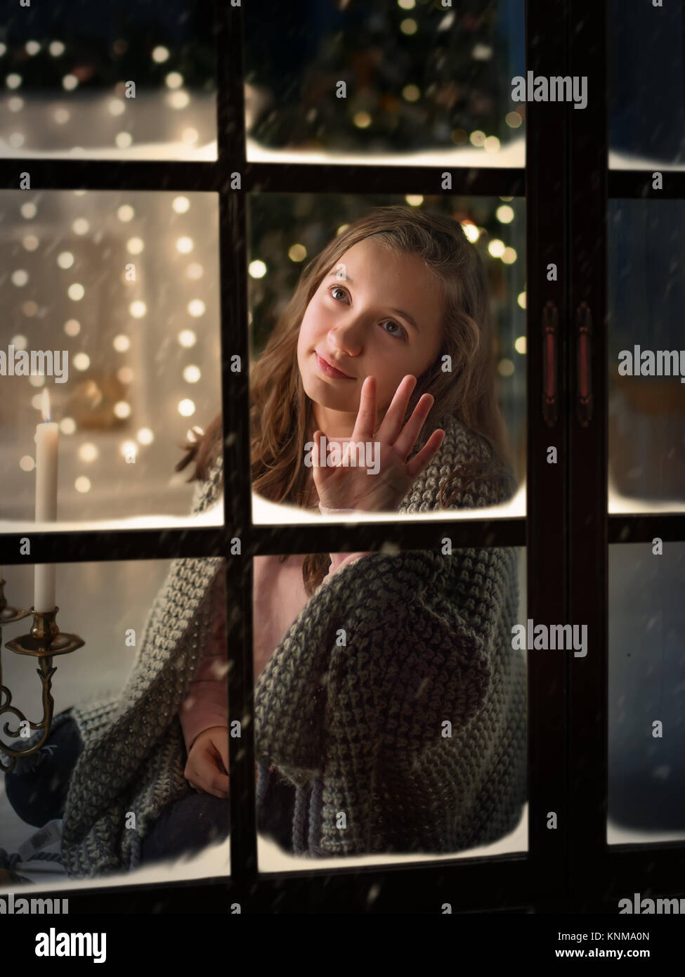 Jolie fille à l'extérieur de la fenêtre à son domicile en prévision de l'année nouveau miracle. Banque D'Images