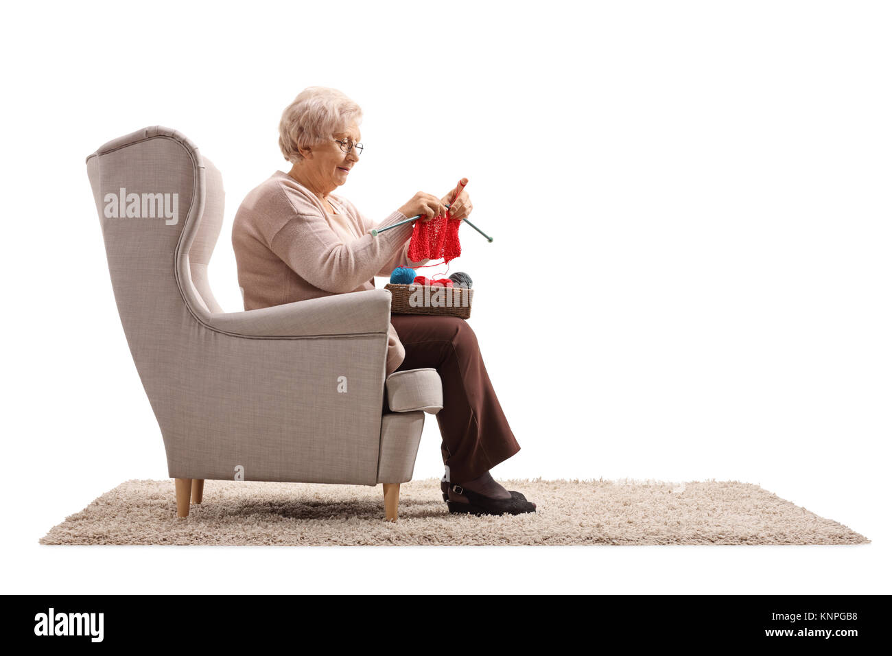 La haute dame assise dans un fauteuil et de tricot isolé sur fond blanc Banque D'Images