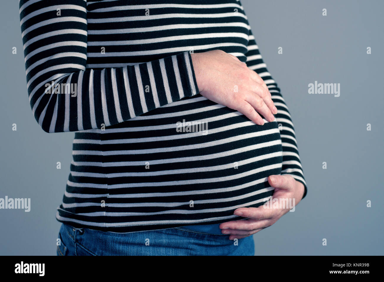Close-up of pregnant woman with hands over ventre sur fond gris clair Banque D'Images