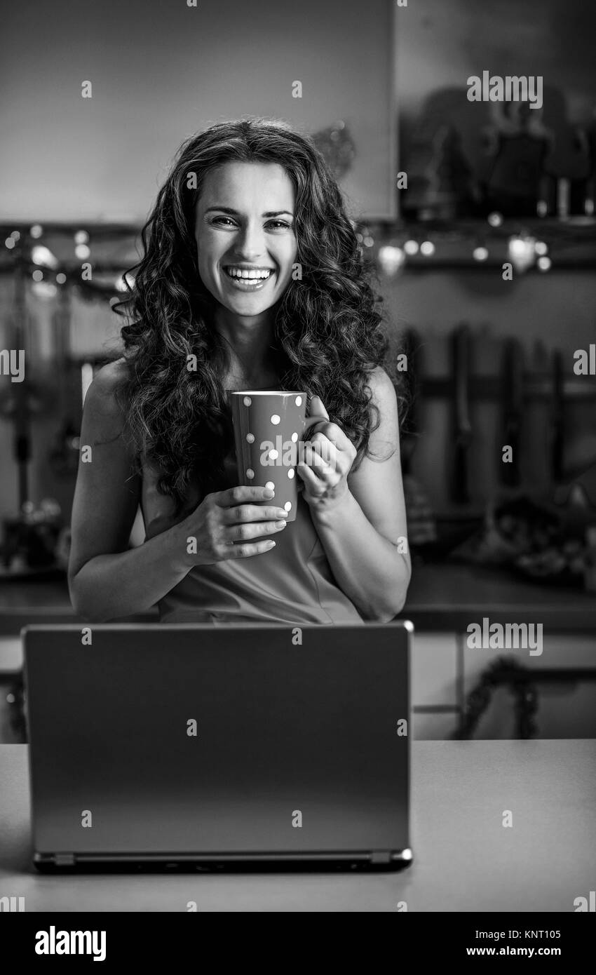 Happy housewife avec une tasse de chocolat chaud à l'aide d'ordinateur portable en cuisine Décoration de Noël Banque D'Images