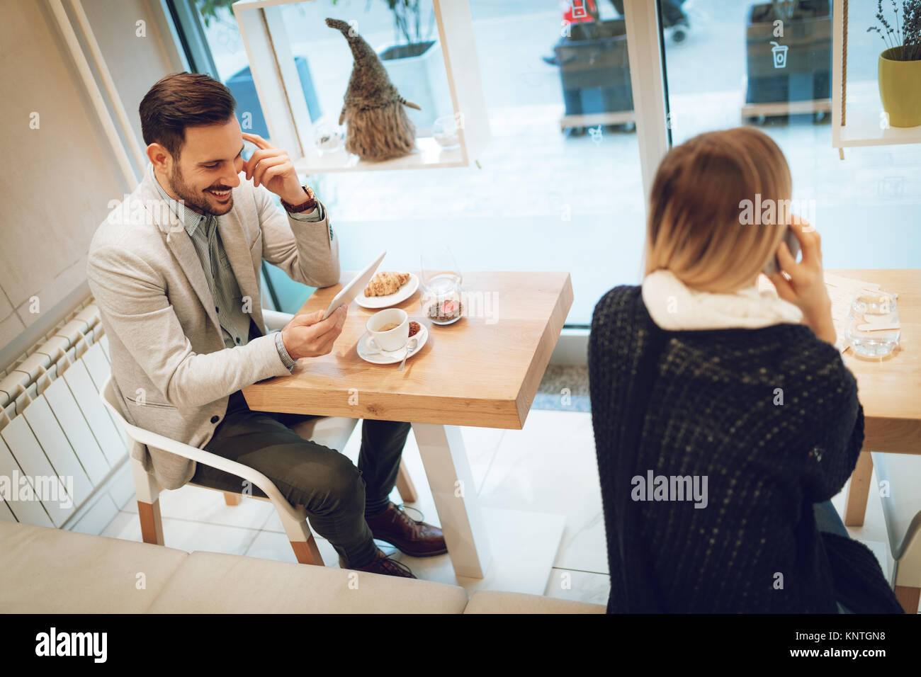 Les jeunes gens d'affaires sur une pause dans un café. Smiling man surfer sur l'internet à tablette numérique et prendre le petit-déjeuner. Femme à l'aide de votre smartphone. Selective Banque D'Images