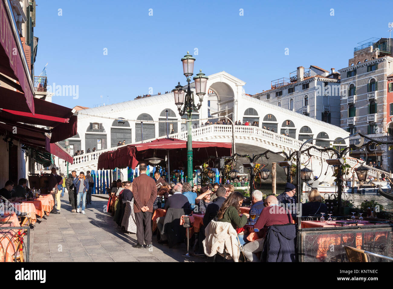 Les gens assis à des tables de restaurant manger midi sous le pont du Rialto, ou Ponte di Rialto, Grand Canal, San Polo, Venise, Italie Banque D'Images
