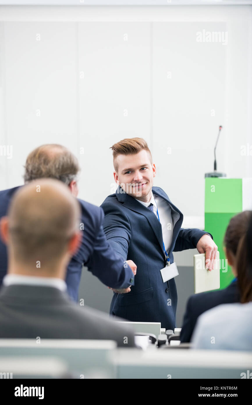 Confident businessman shaking hands with male colleague in lecture hall Banque D'Images