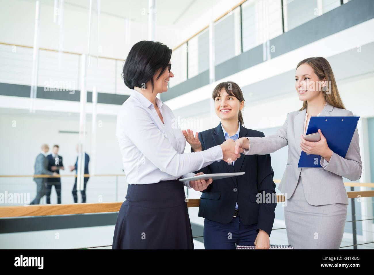 Happy female colleagues shaking hands while standing in office Banque D'Images