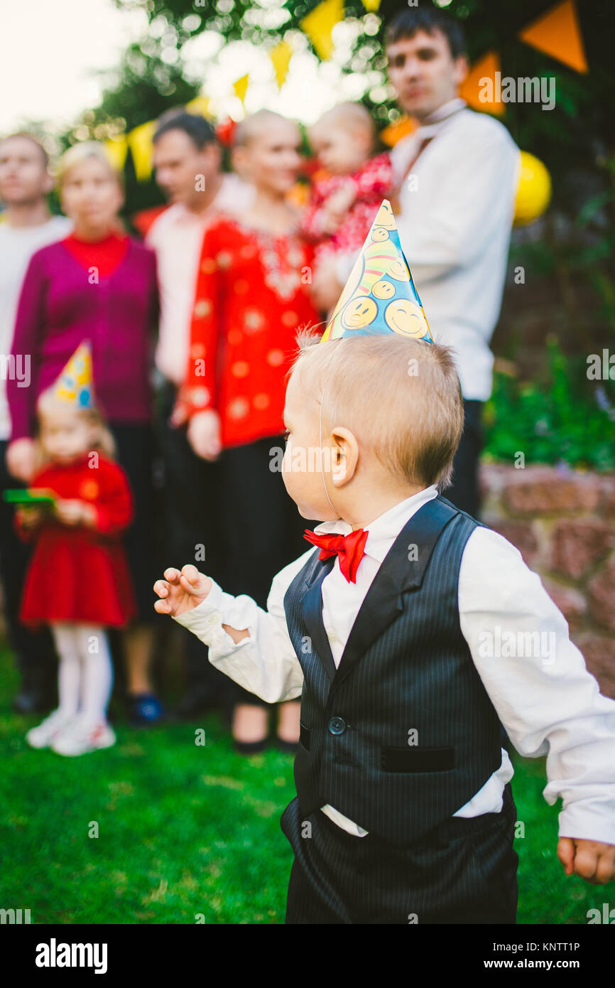 Bébé garçon seul anniversaire en costume avec gilet noir, chemise blanche  et rouge papillon sur l'arrière-plan d'une foule de gens, des invités lors  d'une maison de vacances dans la cour de la