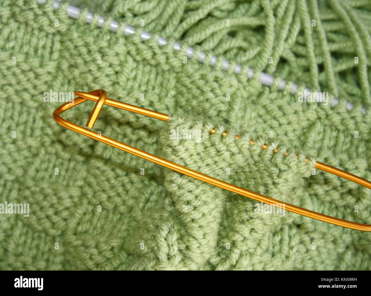 Corbeille tricoté modèle sur des aiguilles à tricoter en laine couleur vert sauge. Porte-croix en place au large de marquage de points supplémentaires à l'unira plus tard Banque D'Images
