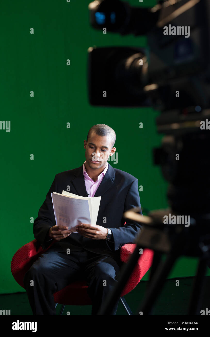 Un présentateur de télévision siège seul, la lecture à travers des scripts avant un enregistrement dans un studio de télévision écran vert Banque D'Images