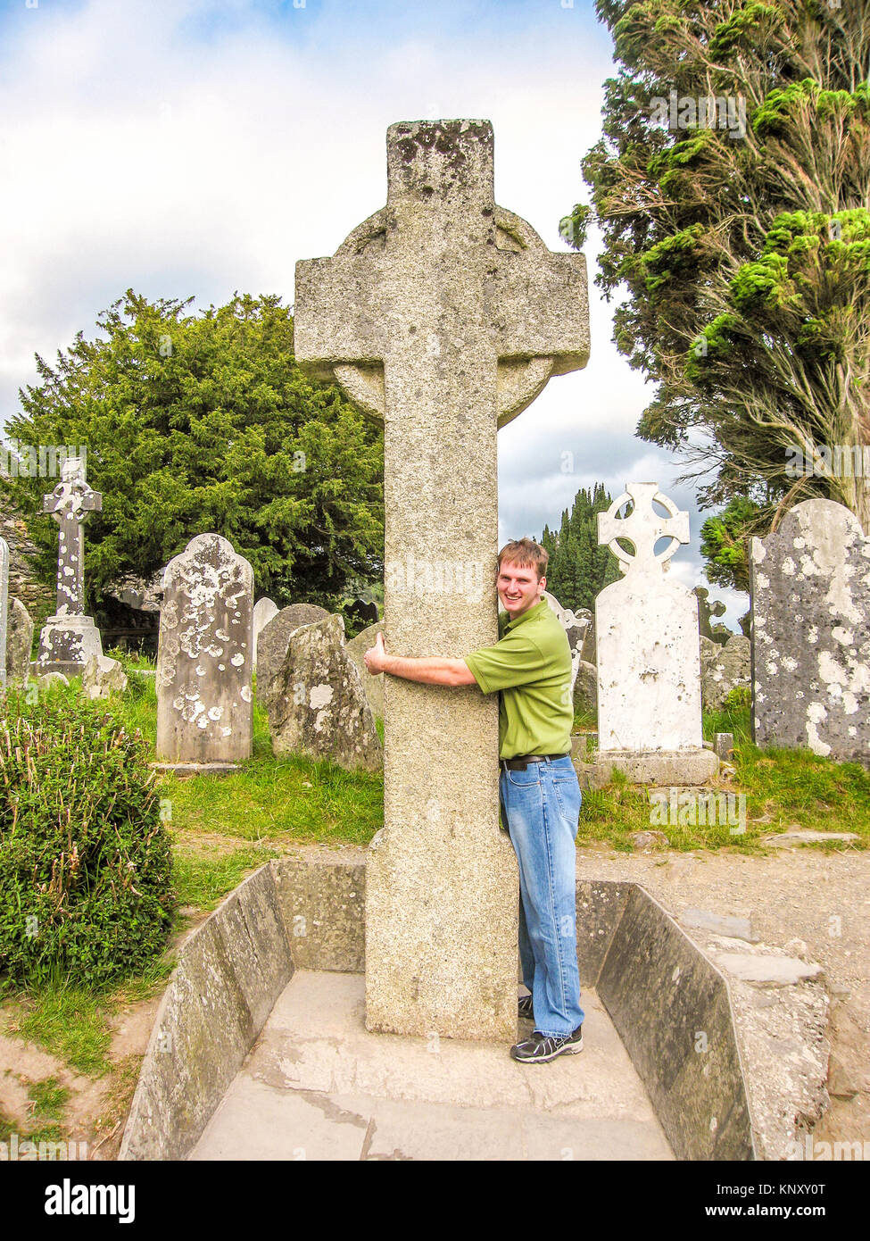 Enveloppement touristiques ses bras autour de St. Kevin's High Cross, Glendalough, dans le comté de Wicklow, Irlande, vers 2007. Glendalough est un des premiers chrétiens sett monastique Banque D'Images