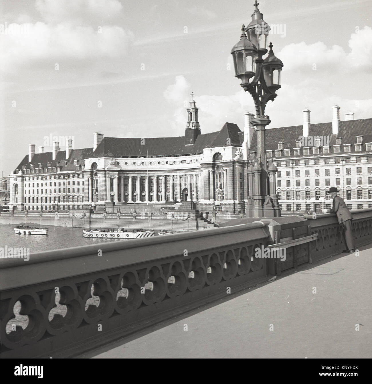 Années 1950, historiques, l'homme debout sur le pont de Westminster, Londres, à la recherche sur la Tamise et à l'impressionnante du County Hall, bâtiment de l'ancien quartier général de la Greater London Council (GLC) à sa droite, sur la rive sud. Banque D'Images