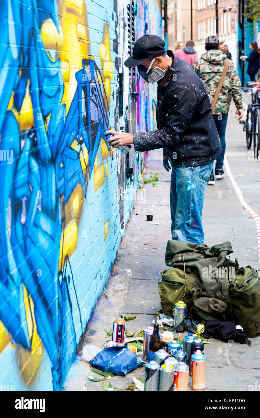 Le Graffiti artiste de rue portant un masque respirateur de pulvériser les murs en Fleur Street, London, UK Banque D'Images