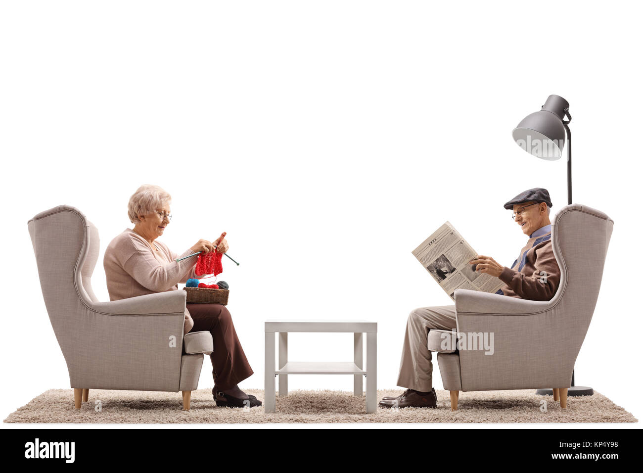 Les aînés assis dans un fauteuil avec l'un d'entre eux le tricot et l'autre lisant un journal isolé sur fond blanc Banque D'Images