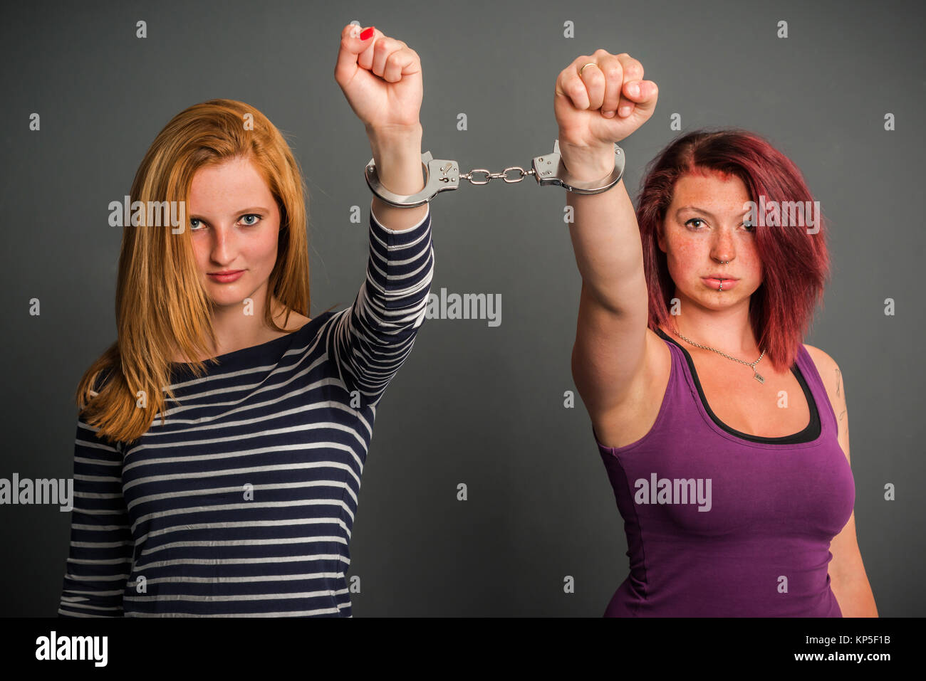 Deux femmes en colère reliées par une paire de menottes, fist, blonde et  brune, rouge sur fond gris Photo Stock - Alamy