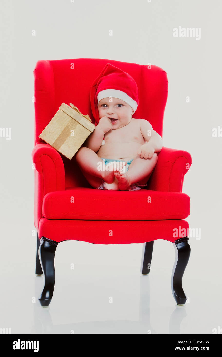 Bébé, 4 Monate, Weihnachtsmuetze und mit sitzt auf einem roten Meteo Contactez-Stuhl - Noël bébé assis sur une chaise rouge Banque D'Images