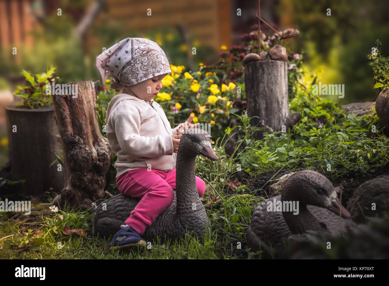 Cute baby girl playing in fairy floraison jardin en campagne avec goose parmi de belles fleurs en été jour symbolisant l'enfance heureuse Banque D'Images