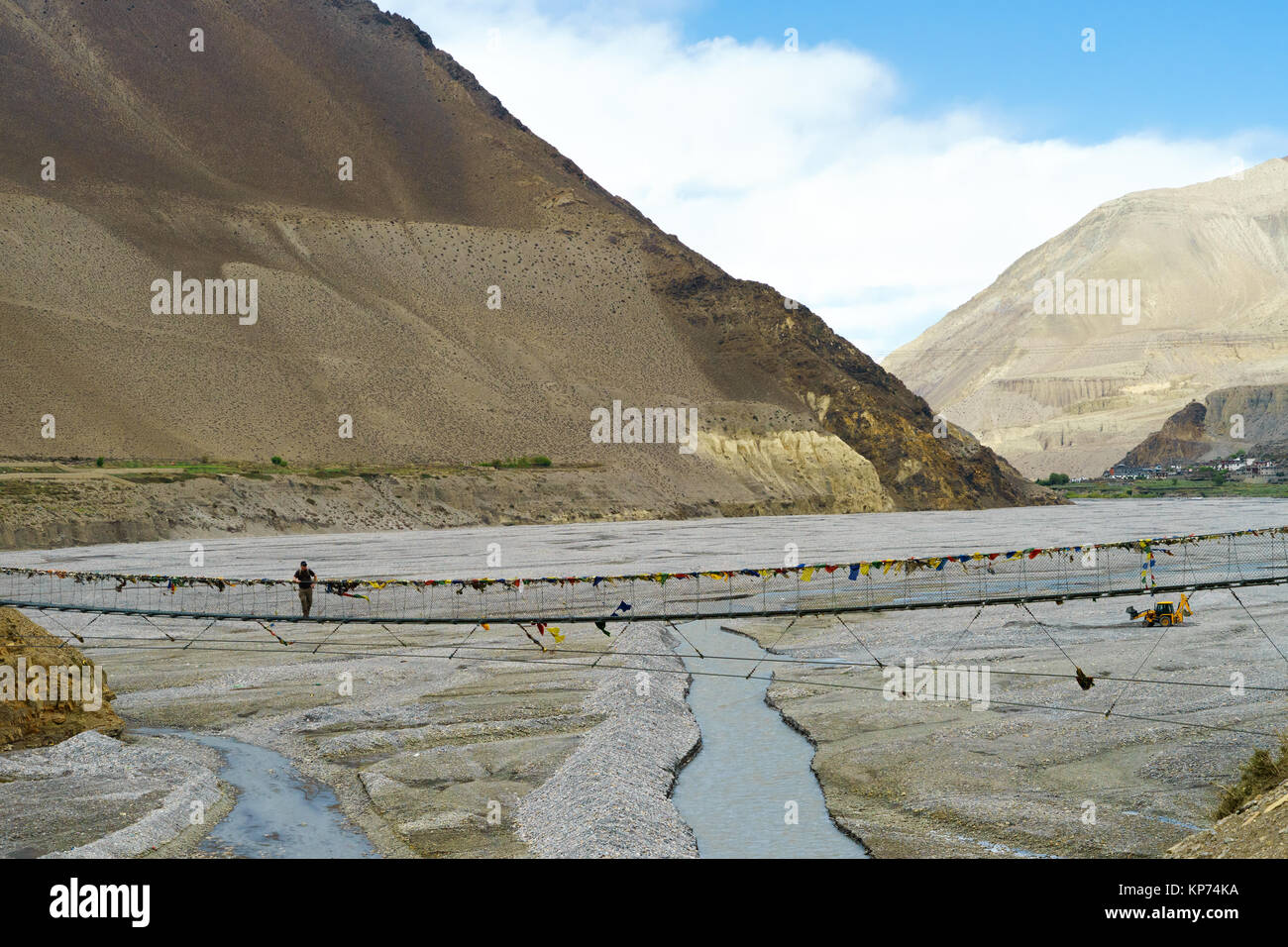 Trekker debout sur un pont suspendu traversant la rivière Kali Gandaki. Ville de Kagbeni visible dans la distance, la région de Mustang (Népal). Banque D'Images
