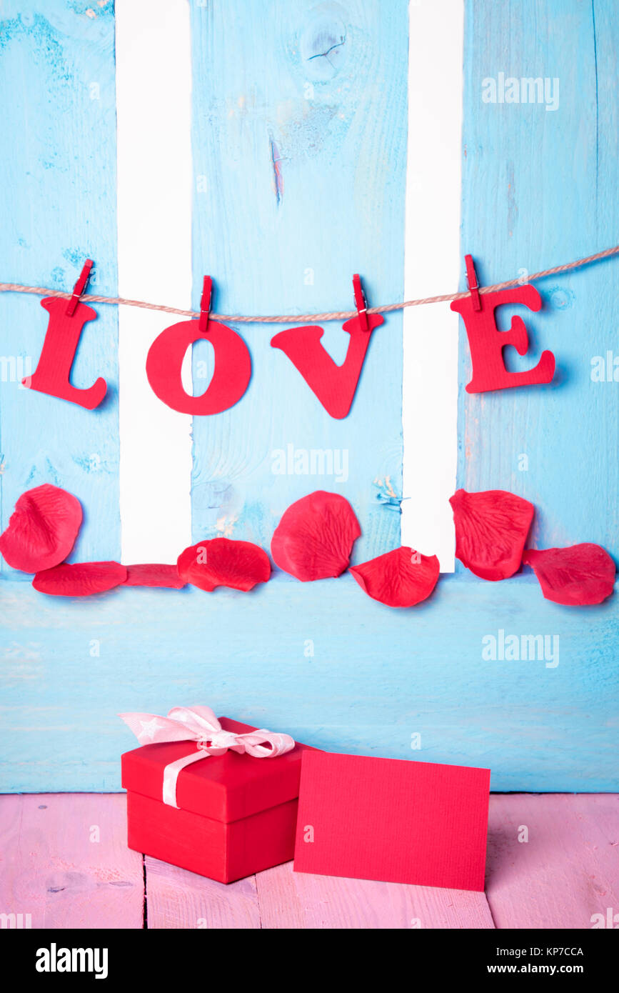 Jolie boîte cadeau rouge avec un message vide près de carte et il le mot amour écrit en lettres papier rouge attaché à une chaîne, sur une clôture en bois bleu. Banque D'Images