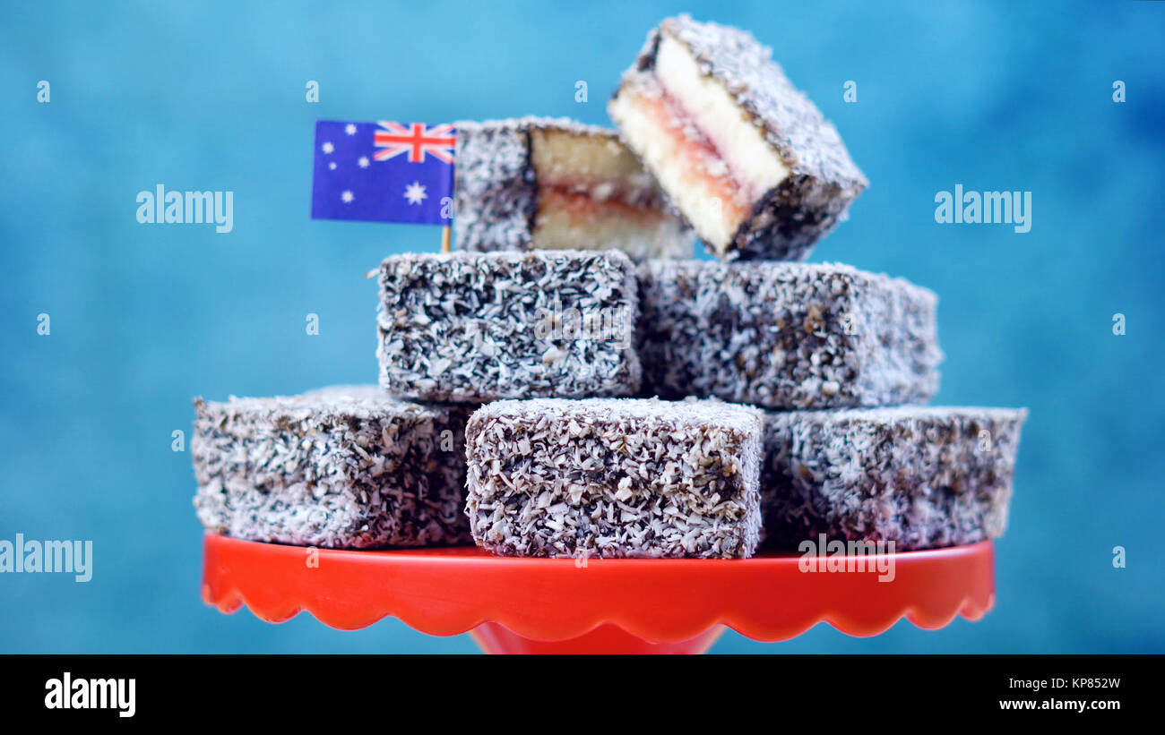 Cuisine de fête traditionnels australiens emblématiques, gâteau Lamington, sur un fond rouge, blanc sur fond bleu. Banque D'Images