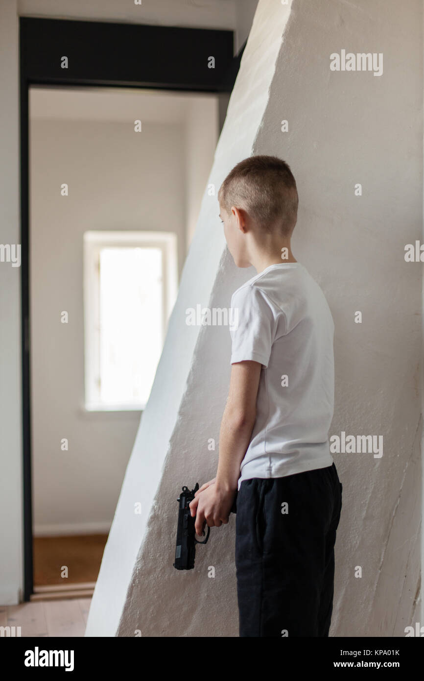 Boy Holding Gun attendant quelqu'un derrière le mur Banque D'Images