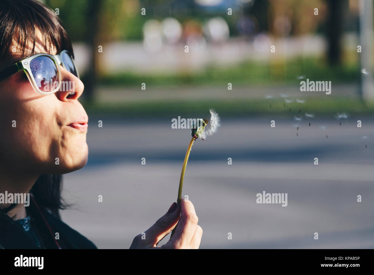 Fille avec sunglases soufflant un pissenlit Banque D'Images