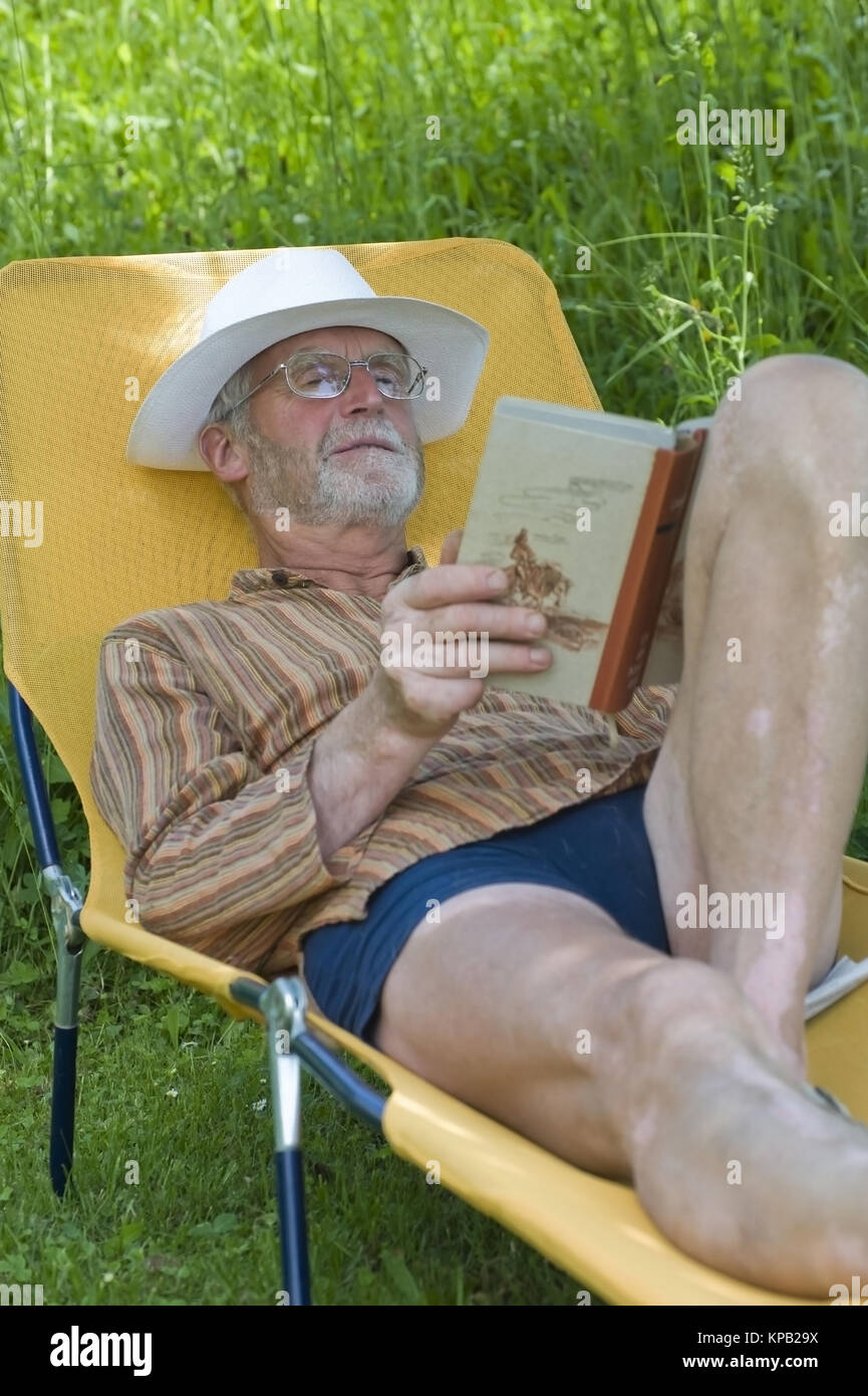 Communiqué de modèle, Pensionist, 65 +, liegt auf Liegestuhl im Garten und liest ein Buch - pensionné allongé sur un transat et la lecture d'un livre Banque D'Images