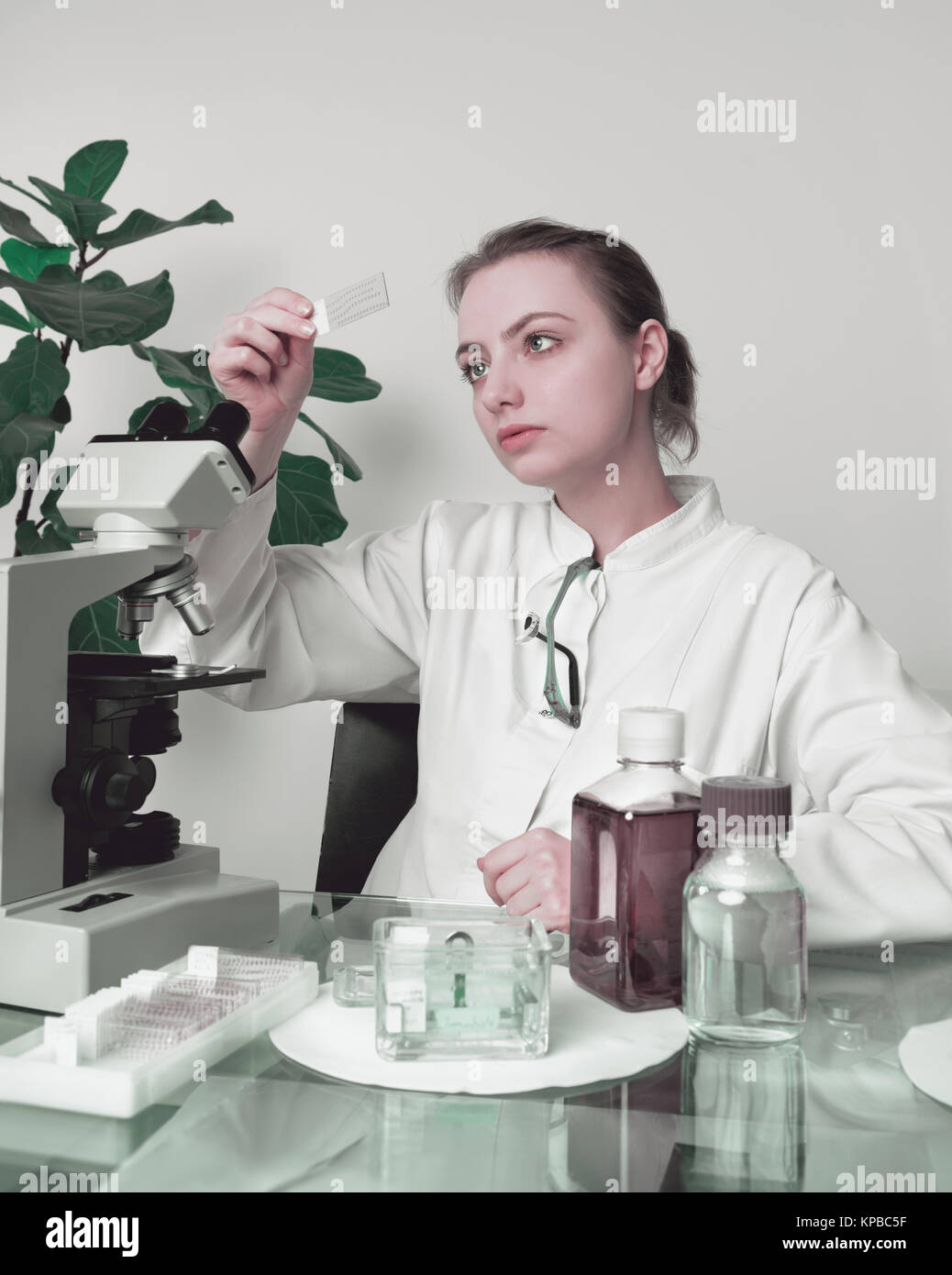Jeune femme microscopiste à manteau blanc sélectionne un échantillon de tissu pour analyse microscopique Banque D'Images