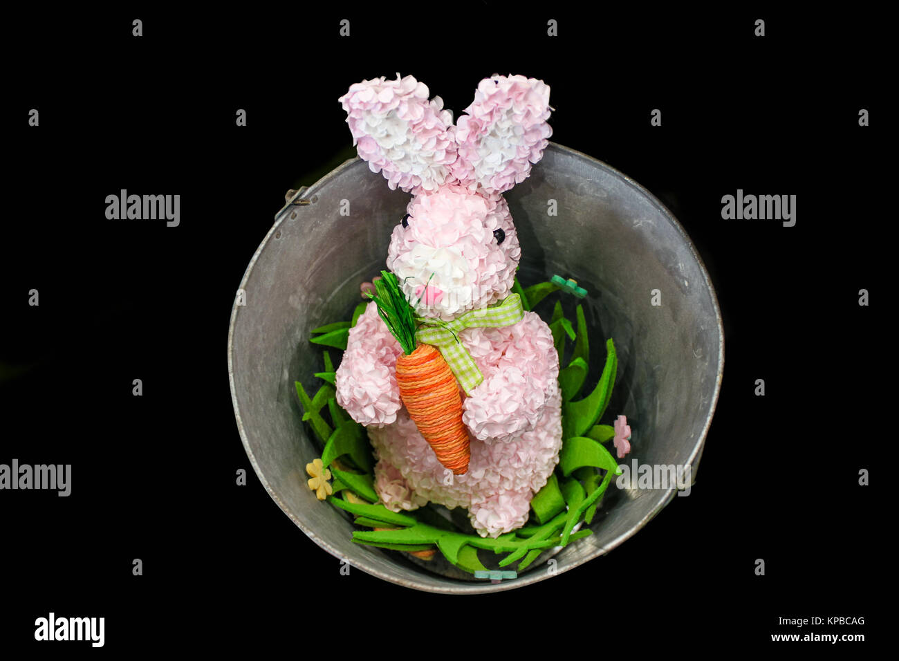 Lapin de Pâques rose fabriqué à partir de pétales de fleurs avec cour carotte dans un seau avec des fleurs isolé sur fond noir Banque D'Images