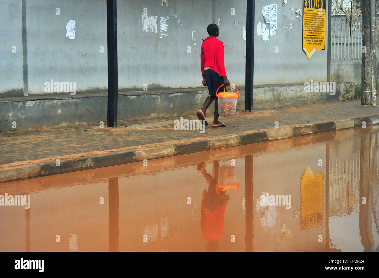 Un homme portant un seau du Mozambique se reflète dans l'eau brune. Banque D'Images
