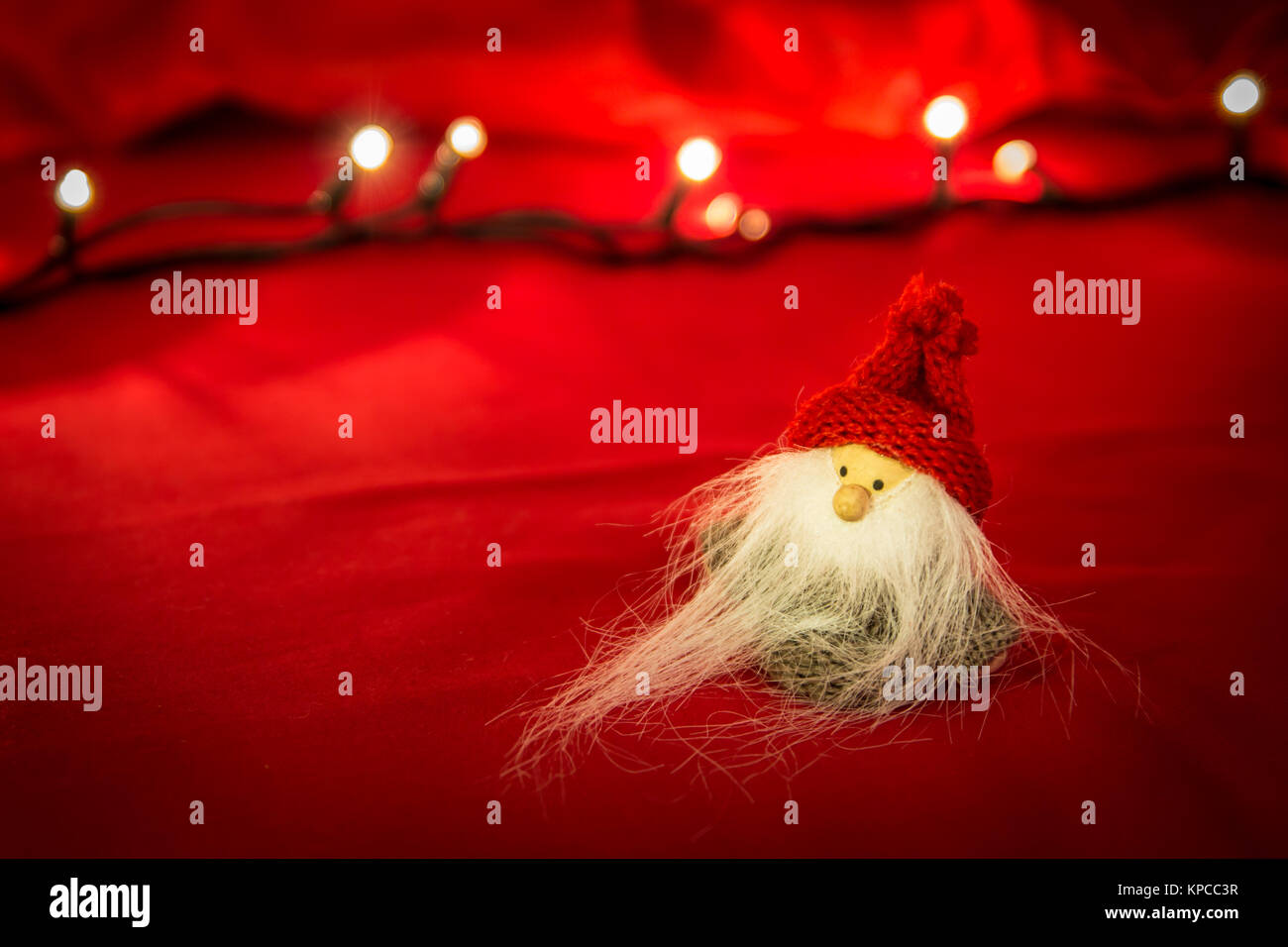 Gros plan du Père Noël mignon puppet avec longue barbe blanche, Noël isolé. Fond tissu rouge et Lumières floues Banque D'Images