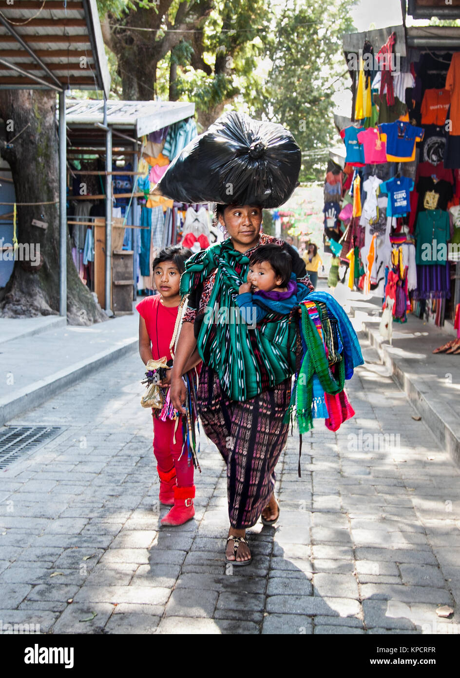 PANAJACHEL, GUATEMALA-DEC 24, 2015 : : Guatamalian femme avec deux enfants transporter sur sa tête grand sac noir le Déc 24, 2015 à Panajachel, Guatemala. Banque D'Images