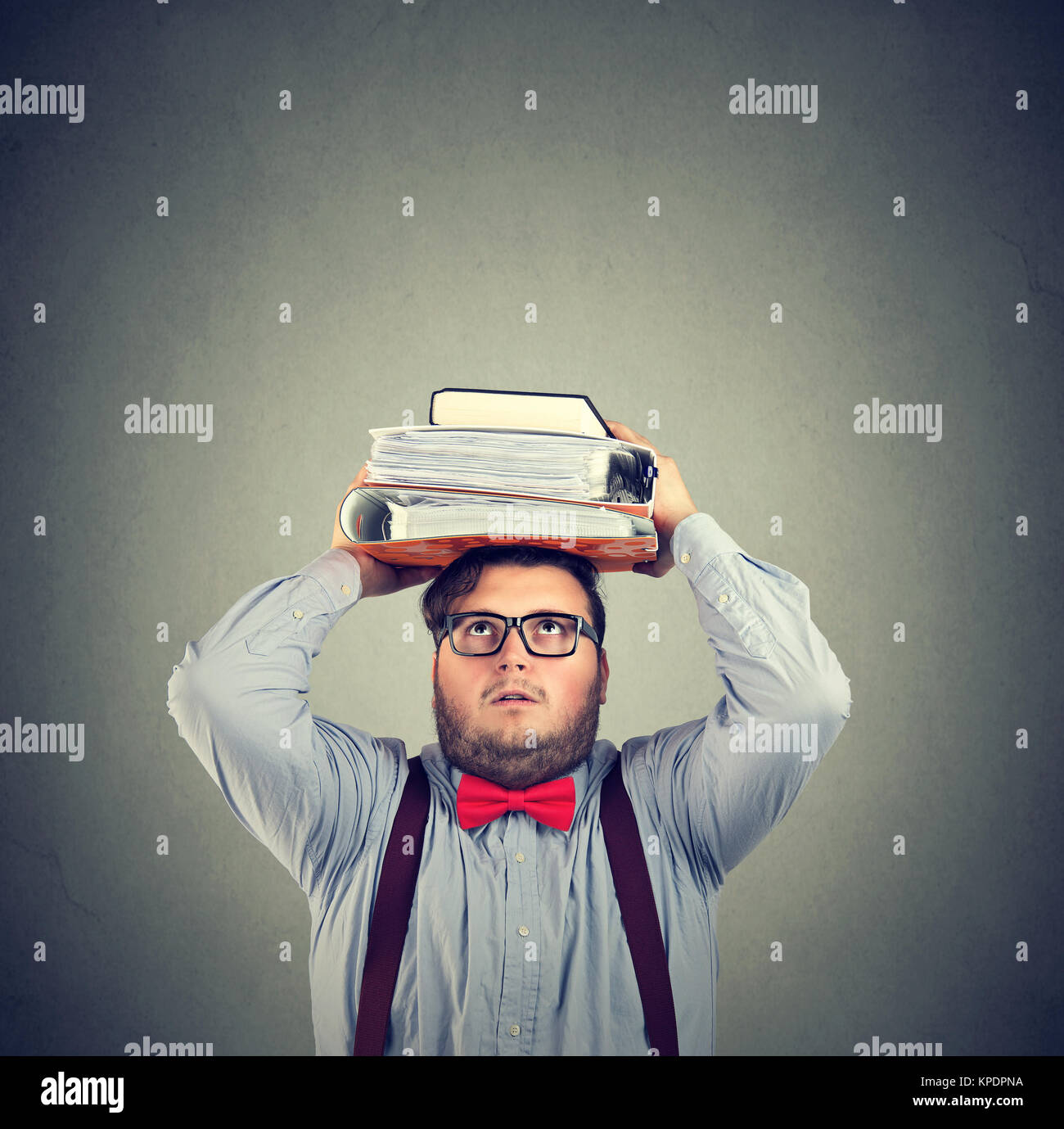 L'Homme à lunettes officielles posant avec des livres lourds sur la tête à la recherche avec des études terrifiés. Banque D'Images