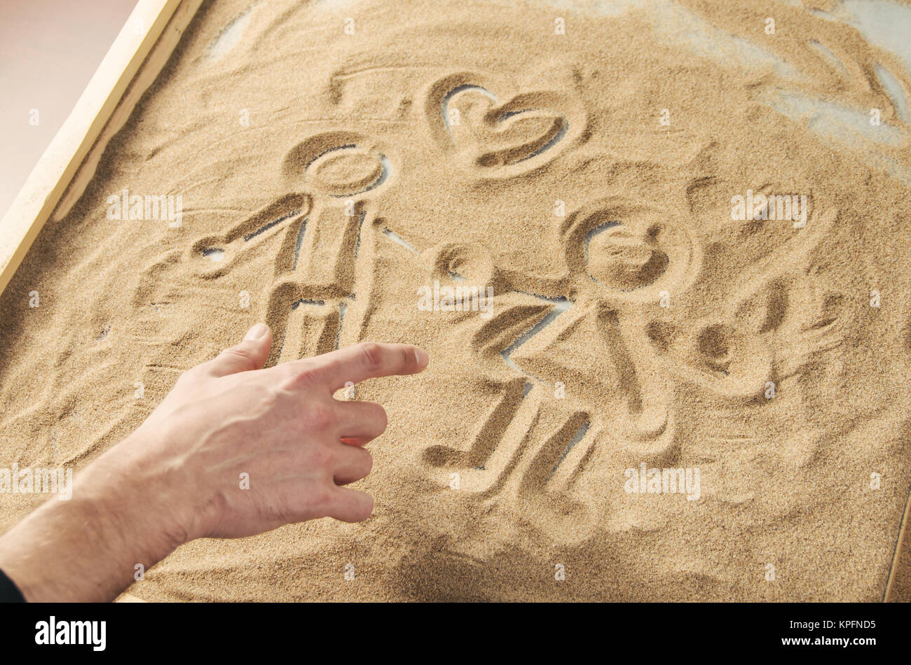 Un homme attire par son doigt sur le sable les figures de l'homme et de la femme avec le symbole du cœur au-dessus d'eux Banque D'Images