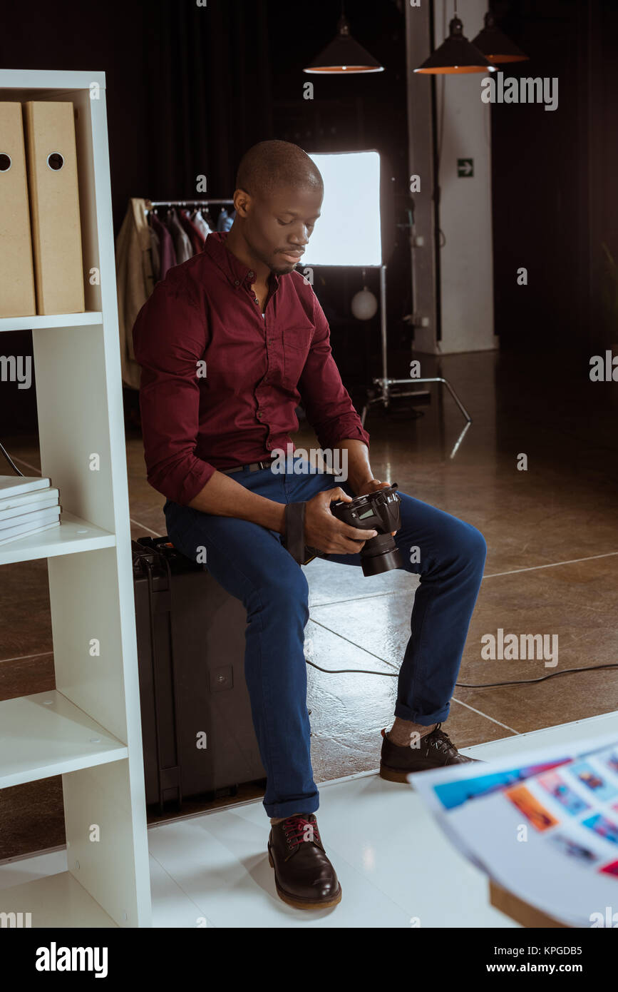 African American photographe à la recherche de photo appareil photo en mains tout en choisissant in studio Banque D'Images