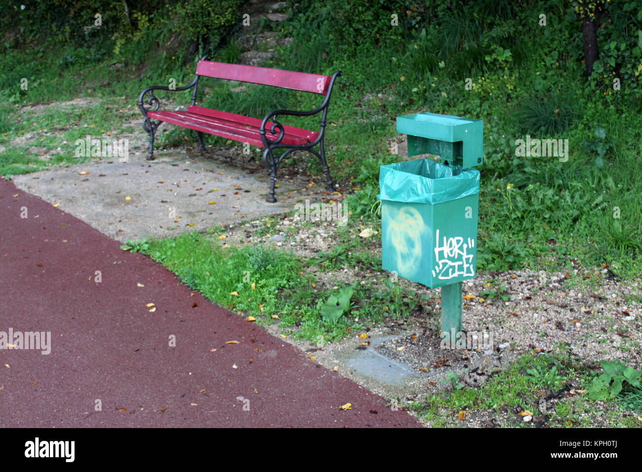 Corbeille métal vert de graffiti et sac en nylon douce à côté de banc en bois avec pieds en fer forgé, et entouré de trottoir pavé uncut haut gra Banque D'Images