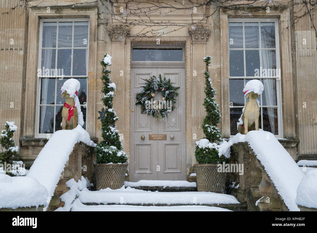 Chien de Noël et décoration guirlande porte des statues dans la neige à l'extérieur d'une maison de ville à Chipping Campden, Cotswolds, Gloucestershire, Angleterre Banque D'Images