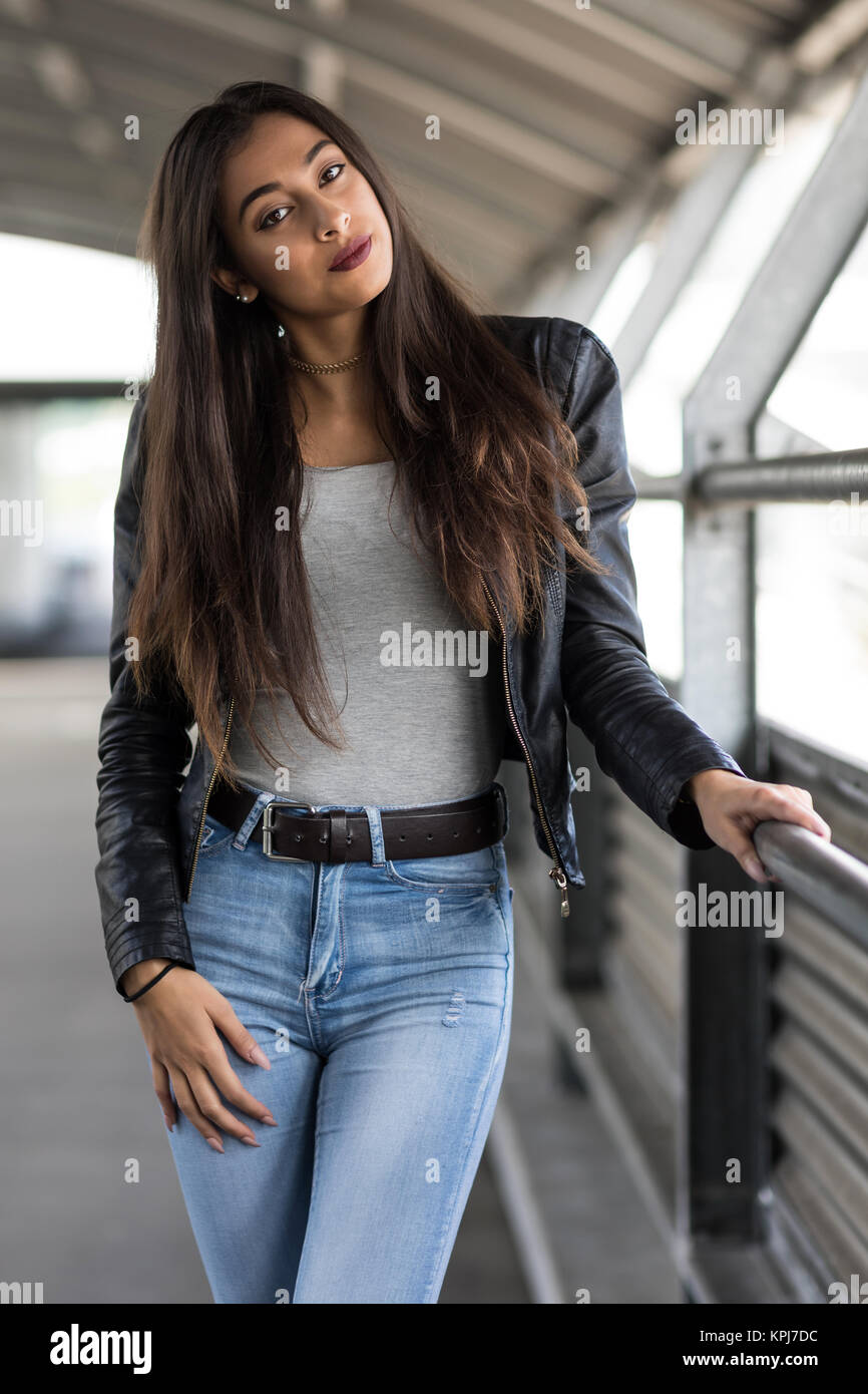 Jeune femme avec de longs cheveux bruns en jeans et blouson de cuir Banque D'Images