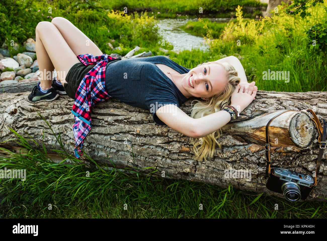 Portrait d'une jeune femme avec de longs cheveux blonds portant sur un journal dans un parc ; Edmonton, Alberta, Canada Banque D'Images