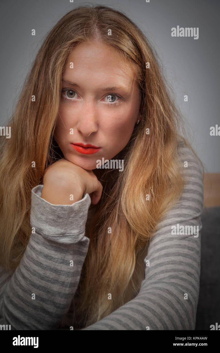 Jeune femme avec de longs cheveux blonds qui pose pour l'appareil photo tout en posant son menton sur sa main ; California, United States of America Banque D'Images