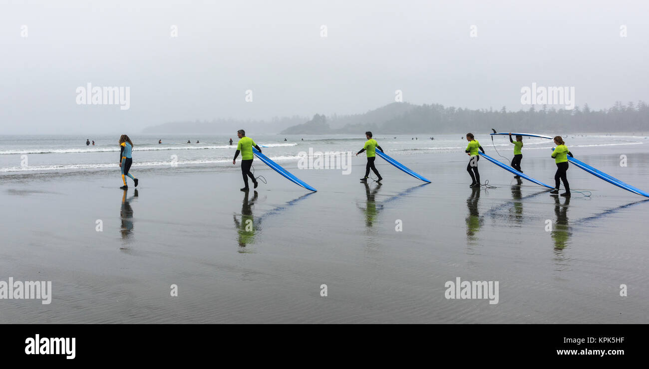 Un groupe de personnes sur la plage humide portant des t-shirts et de transporter les planches de bleu, Cox Bay Beach, parc national Pacific Rim, l'île de Vancouver Banque D'Images